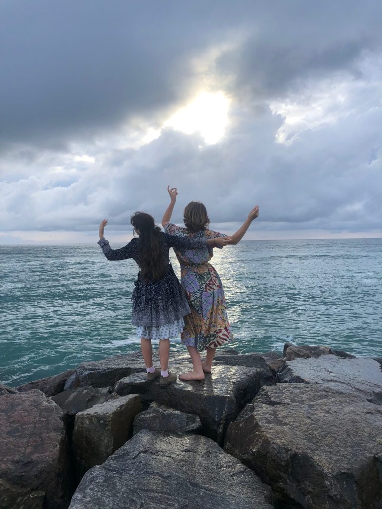 Two women raising their arms joyfully by the sea – Do-In online sessions